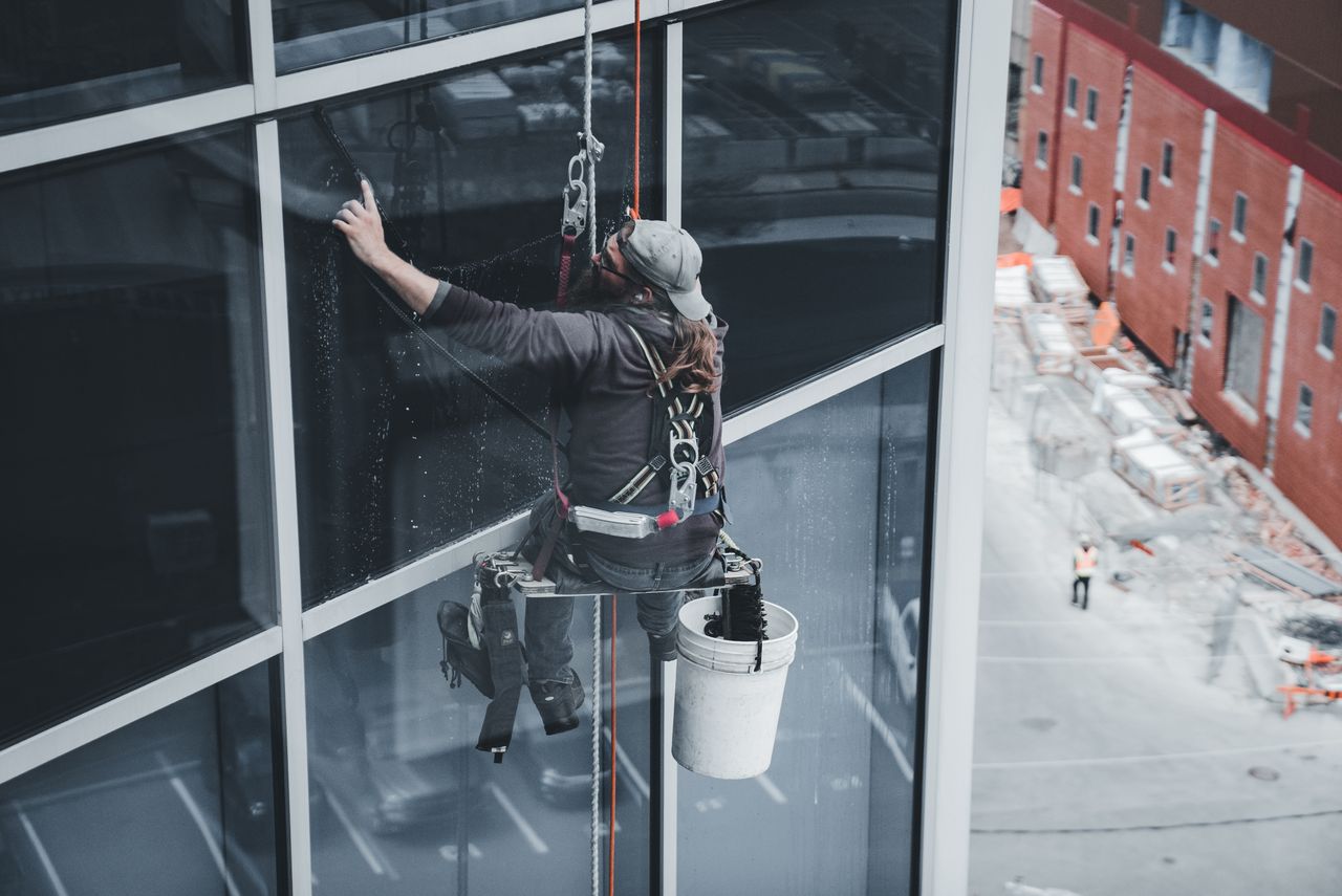 team-03 A worker cleaning skyscraper windows with a harness in an urban setting.
