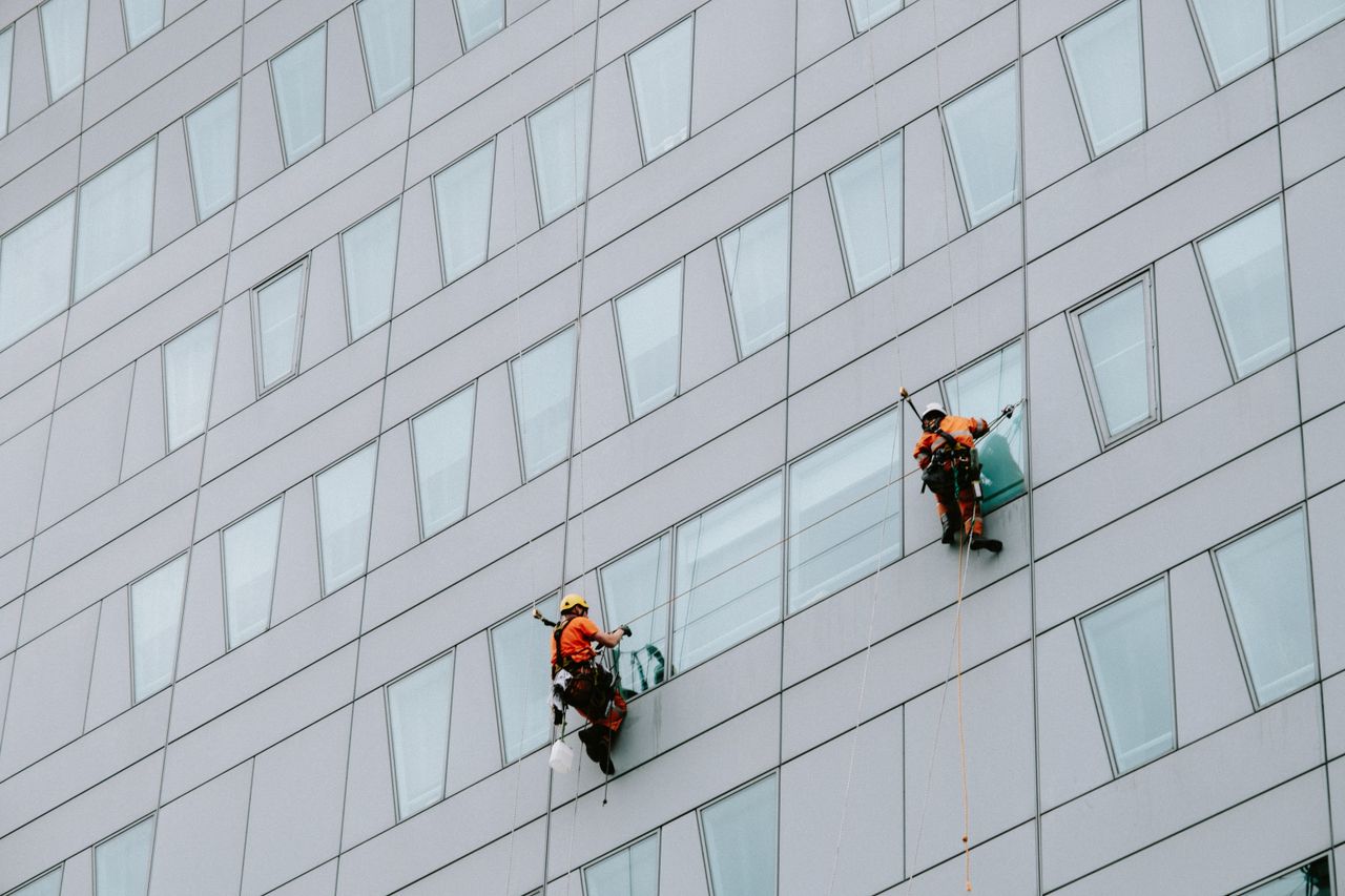 team-02 High-rise window washers in safety gear cleaning a skyscraper facade.